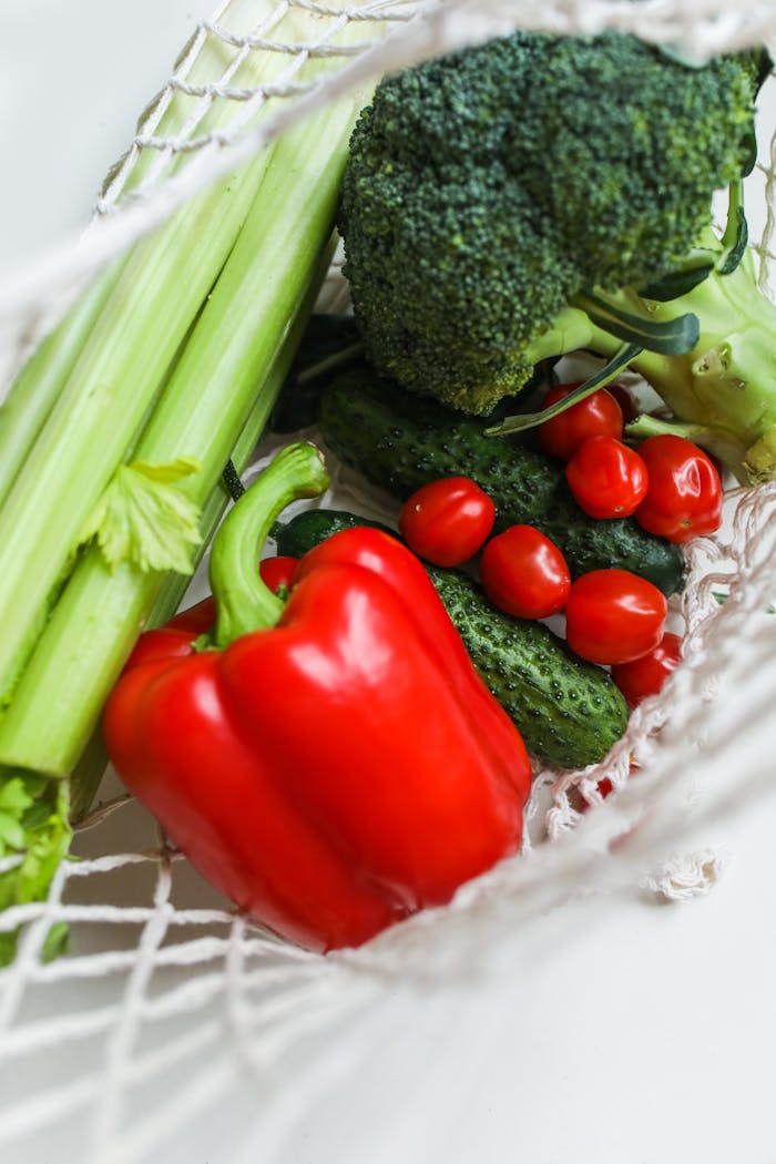 A vibrant mix of fresh vegetables including broccoli, bell peppers, and cucumbers in a net bag.