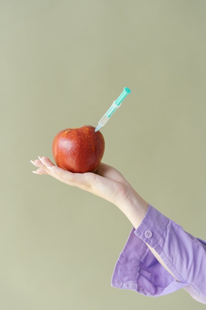 Creative photo of an apple with a syringe, symbolizing possible genetic modification.