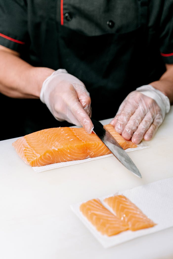 A chef slicing fresh salmon fillets with precision for sushi preparation, showcasing culinary skills.